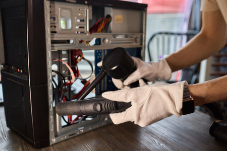 A man cleans a computer case with a vacuum in a bright room, stressing workspace tidiness