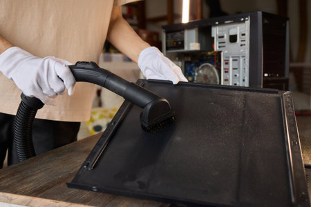 A man cleans a computer case with a vacuum in a bright room, stressing workspace tidiness
