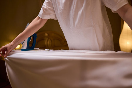 A person meticulously ironing clothes at home, ensuring all garments are neat and well cared forの写真素材