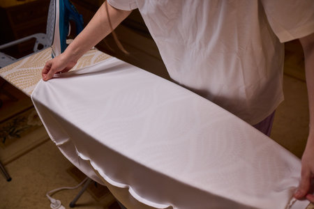 A person meticulously ironing clothes at home, ensuring all garments are neat and well cared for