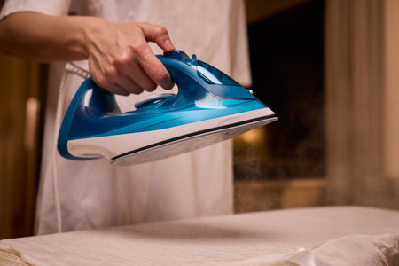 A person meticulously ironing clothes at home, ensuring all garments are neat and well cared forの写真素材