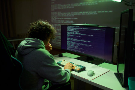 A young programmer codes intently in a dark setting, immersed in his work and creativityの写真素材