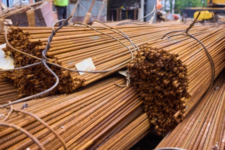 Stacked steel rods are prominently observed at a bustling construction site in progressの写真素材