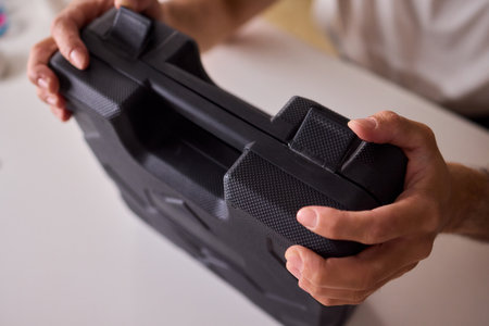 A person is holding a sleek black carrying case while positioned at a clean table setting
