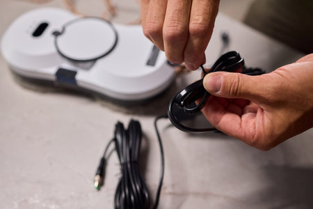 Hands Skillfully Organizing a Charging Cable Neatly in Proximity to a Device Across the Tableの写真素材