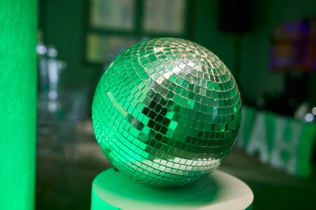 Green illuminated reflective mosaic, Velvet table illuminated by radiant glowing ball, Celebratory party centerpiece with luminous mosaic mirror ball and velvet tableの写真素材