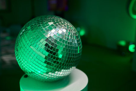 Green illuminated reflective mosaic, Velvet table illuminated by radiant glowing ball, Celebratory party centerpiece with luminous mosaic mirror ball and velvet tableの写真素材