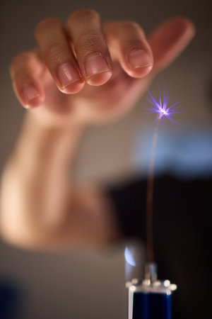 Hands manipulating metal spheres generate vibrant electrical plasma display, Laboratory scene...