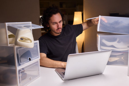 Individual systematically records shoe information on computer in workspace, Person carefully inputs sneaker details into spreadsheet within tidy home office environmentの写真素材