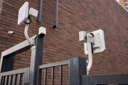 Urban security surveillance, Industrial style gate camera system, Surveillance units installed on brick structures, Perimeter monitoring with visible cables and bracketsの写真素材