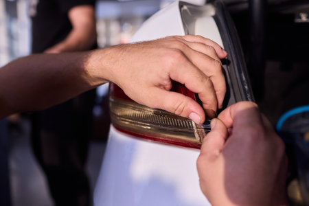 Hands fixing car light, Closeup of hands replacing taillight under open trunk lid, Individuals collaboratively repairing electrical wiring for vehicle tail light assemblyの写真素材