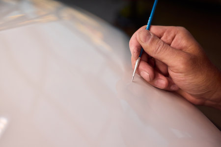Closeup of technician testing automotive paint swatches with fine brush, Precision detailing technician carefully applying paint swatches on car surface in dim workshopの写真素材