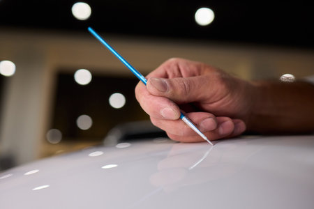 Closeup of technician testing automotive paint swatches with fine brush, Precision detailing technician carefully applying paint swatches on car surface in dim workshopの写真素材