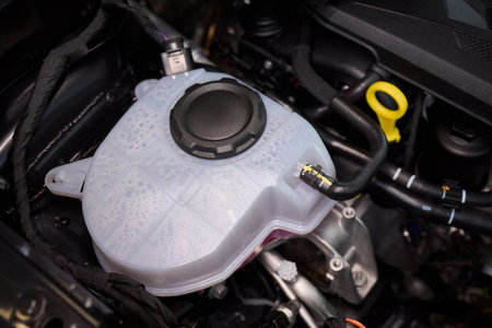 Closeup of coolant container during vehicle maintenance process, Technician topping off coolant reservoir in engine compartment under proper lighting conditionsの写真素材