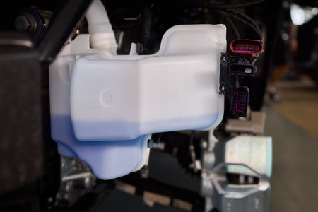 Closeup of coolant container during vehicle maintenance process, Technician topping off coolant reservoir in engine compartment under proper lighting conditionsの写真素材