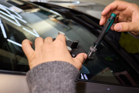 Closeup of technician repairing windshield inside garage, Professional technician employs specialized equipment to mend damaged windshield efficiently and safelyの写真素材