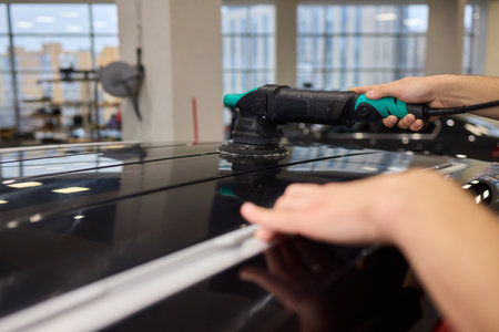 Polishing black car surface thoroughly, Detailed buffing to achieve showroom quality shine, Expert technician uses orbital buffer and foam pad to enhance vehicle glossの写真素材