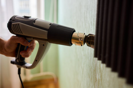 Craftsman carefully detaching acoustic panels indoors, Individual skillfully peels acoustic insulation from wall using heat and precise hand movements for studio setupの写真素材