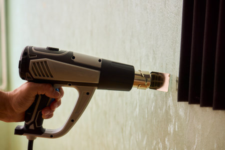 Craftsman carefully detaching acoustic panels indoors, Individual skillfully peels acoustic insulation from wall using heat and precise hand movements for studio setupの写真素材