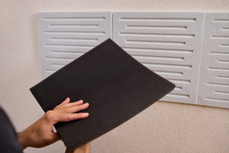 Closeup of foam insulation method, Hand pressing textured acoustic foam onto wall surface, Detailed shot of fingers securing black foam panels on gray wall Comparison of different foam rubber and sound absorption efficiencyの写真素材