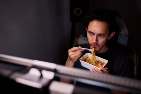 Live streaming snack, Content creator enjoys snack during livestream break, Casual moment captured during evening stream with ambient glow and home studio backgroundの写真素材