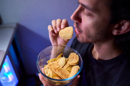 Programmer enjoying late night snack, Individual working alone in home office environment, Solitary male professional grubbing on sandwich during late hours at his deskの写真素材