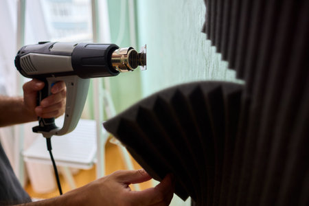Craftsman carefully detaching acoustic panels indoors, Individual skillfully peels acoustic insulation from wall using heat and precise hand movements for studio setupの写真素材