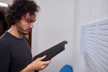 Closeup of foam insulation method, Hand pressing textured acoustic foam onto wall surface, Detailed shot of fingers securing black foam panels on gray wall Comparison of different foam rubber and sound absorption efficiencyの写真素材