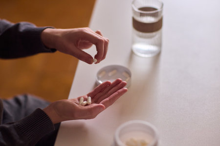 Medicinal moment captured, Calm scene depicting nighttime wellness with pills and water, Gentle indoor setting featuring hands managing pills during peaceful evening routineの写真素材