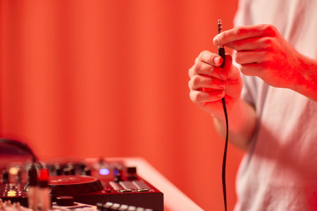 DJ setup closeup, Close view of audio connection process during live performance, Detailed image capturing technician connecting audio cables to mixer with ambient lightingの写真素材