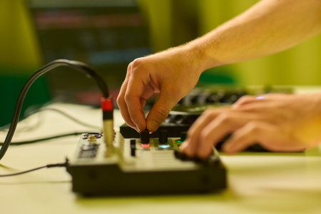 Closeup of tactile controls and vibrant patch cords in studio, Adjusting analog sequencing equipment with bright cables and warm ambient lighting in home studioの写真素材