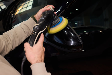 Polishing black car surface thoroughly, Detailed buffing to achieve showroom quality shine, Expert technician uses orbital buffer and foam pad to enhance vehicle glossの写真素材