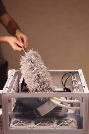 Cleaning computer components with brush. Closeup of dusty electronics being cleaned. Detailed shot of technician cleaning dust from motherboard and cables with soft lightingの写真素材