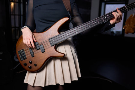 Female bassist rehearsing. Female musician with bass guitar. Female performer practicing in dim studio lighting. Female bassist preparing for performance in moody rehearsal spaceの写真素材
