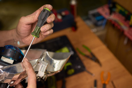 Closeup of technician securing car headlight components. Focused shot showing technician carefully attaching and securing headlamp wiring to metal support with precisionの写真素材