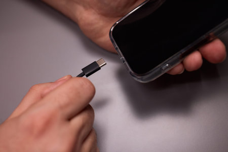 Person repairing phone by testing headphone jack connection on matte surface. Detailed view of user troubleshooting audio port on modern smartphone with headphonesの写真素材