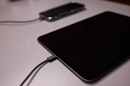 Tablet and phone charging scene. Smart devices plugged in on textured desk at night. Charging tablet...