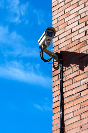 Security surveillance camera on brick wall. Blue sky background