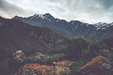 Mountain landscape with snow-capped mountains on horizon. Dark cloudy sky.の写真素材