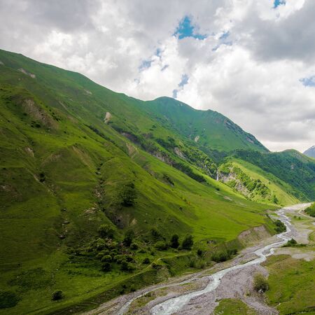 Beautiful mountains landscape with river in grass valley. Cloudy sky rocks view. Nature backgroundの写真素材