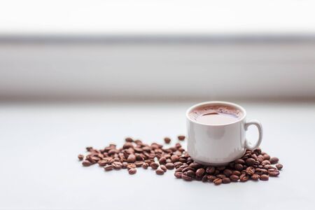 Scattered coffee beans and cup on white windowsill. Morning breakfast concept backgroundの写真素材