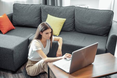 Young woman with modern laptop sitting on sofa at home. Happy girl browsing through the internet during free time..の写真素材