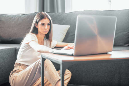 Young woman with modern laptop sitting on sofa at home. Happy girl browsing through the internet during free time ..の写真素材