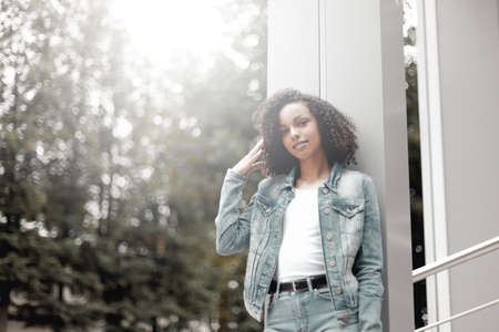 Mulatto black curly girl on street. Sunny summer city. Young woman denim styleの写真素材