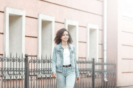 Mulatto black curly girl on street. Sunny summer city. Young woman denim style