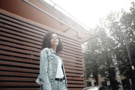 Mulatto black curly girl on street. Sunny summer city. Young woman denim styleの写真素材