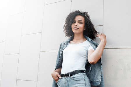 Mulatto black curly girl on street. Sunny summer city. Young woman denim styleの写真素材