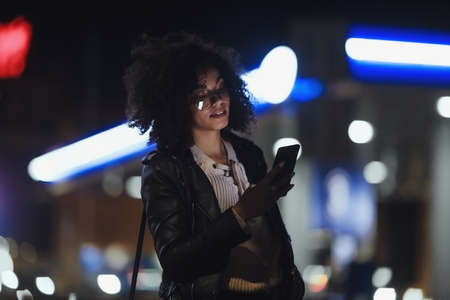 Portrait of young cute curly afro american girl. Night city lights. Neon illuminationの写真素材