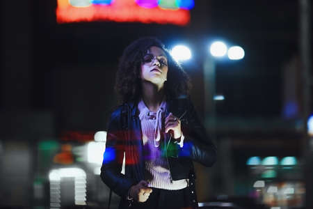 Portrait of young cute curly afro american girl. Night city lights. Neon illuminationの写真素材