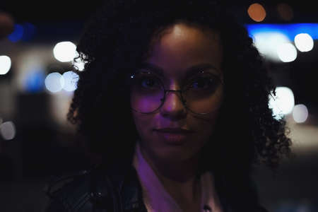 Portrait of young cute curly afro american girl. Night city lights. Neon illuminationの写真素材